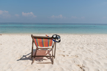 close up a diving mask hanging in a bright colored wooden beach chair on island tropical beach