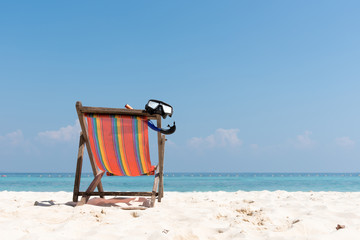 Diving mask hanging in a bright colored wooden beach chair on island tropical beach