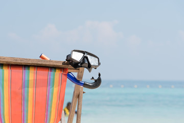 close up a diving mask hanging in a bright colored wooden beach chair on island tropical beach