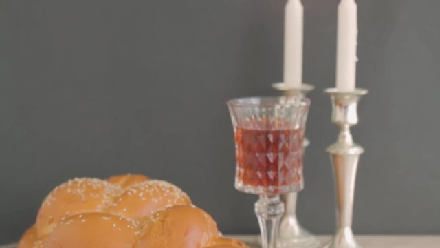 Shabbat or Sabbath kiddush ceremony composition with a traditional sweet fresh loaf of challah bread, glass of red kosher wine and candles on a vintage wood background. Tilt camera action
