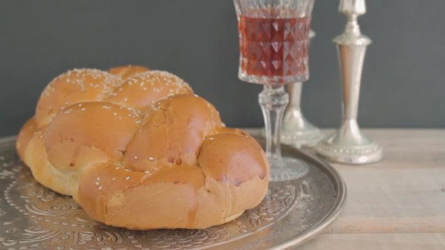 Shabbat or Sabbath kiddush ceremony composition with a traditional sweet fresh loaf of challah bread, glass of red kosher wine and candles on a vintage wood background. Tilt camera action