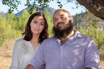 Happy couple sitting close together under a tree looking at the camera