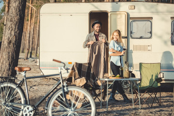 young man wearing warm sweater on his girlfriend near campervan, bicycle on foreground