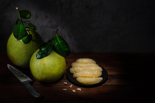 Two pomelos, a plate of pomelo flesh and a knife on the wooden table with light painting effect