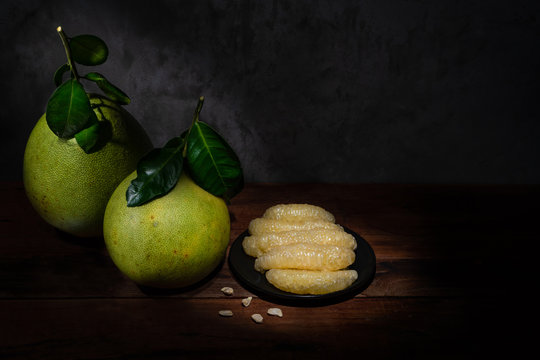 Two pomelos and a plate of pomelo flesh on the wooden table with light painting effect