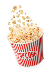Delicious popcorn falling into red paper bucket on white background
