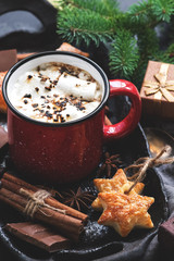 Hot chocolate with marshmallow in a red mug, cinnamon, star anise, cookies, gifts, spruce branches. Christmas background. Selective focus.