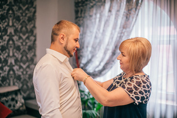Mother is helping with a bow-tie to her son. Dressed and preparing her son for the wedding...