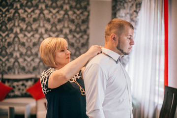 Mother is helping with a bow-tie to her son. Dressed and preparing her son for the wedding...