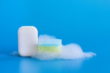 White soap with cleaning sponge and bubbles foam on blue background. Copy space.