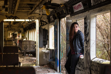 Fototapeta na wymiar portrait Young woman with long grounge red hair and black leather jacket posing in an abandoned trainfull of graffity
