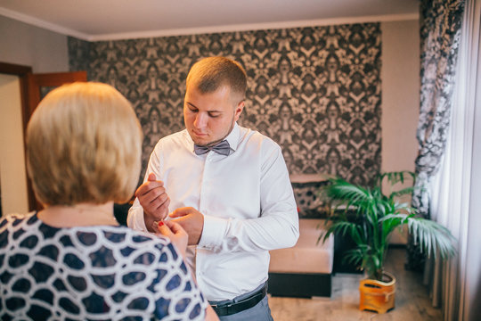 Mother Is Helping With A Bow-tie To Her Son. Dressed And Preparing Her Son For The Wedding Ceremony. The Groom Wears A Jacket And Looking To Mother.