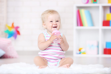 Baby girl sitting on white carpet with bottle