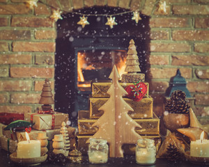 Christmas setting, wooden ornaments, presents and pine cones, tree on the table in front of fireplace with woodburner, star lights and garlands, lit lantern, created snow, selective focus, toned