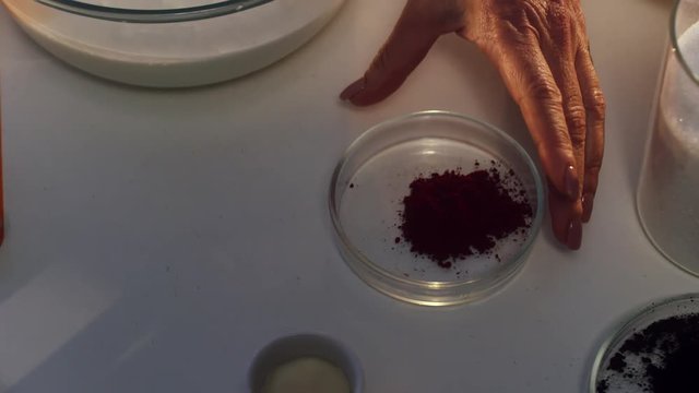 Slow motion of dark red powder in small plate being sprinkled onto sour cream in big glass pan on white table beside dish with strawberries and set of spoons with forks.