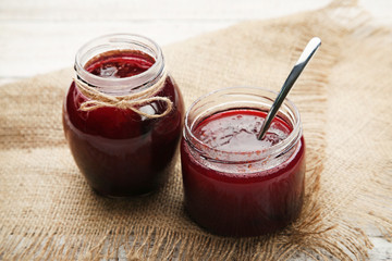 Plum jam in jars with spoon on white wooden table