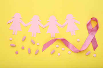 Pink ribbon with pills and paper people on yellow background. Breast cancer concept