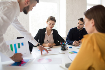 Group of creative people working together on new project. Young girl in shirt and jacket thoughtfully working while spending time in modern office