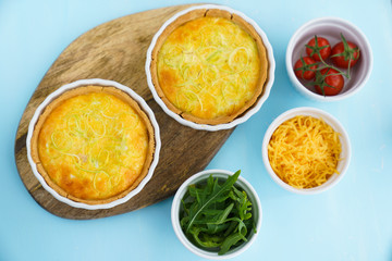 Gluten free leek mini quiches on a wooden board served with fresh rukkola, tomatoes and cheese