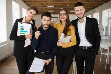Group of young creative people in suits happily looking in camera together while spending time at work in modern office