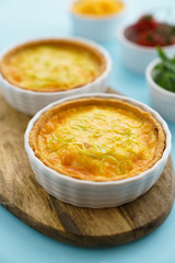 Gluten free leek mini quiches on a wooden board served with fresh rukkola, tomatoes and cheese