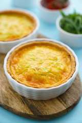 Gluten free leek mini quiches on a wooden board served with fresh rukkola, tomatoes and cheese
