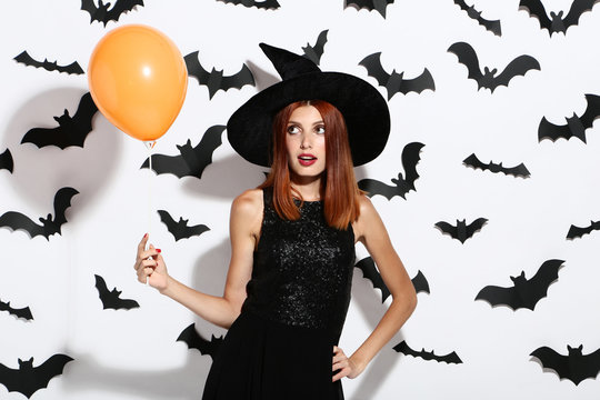 Beautiful redhaired woman with balloons and paper bats on white background