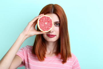 Young redhaired woman with grapefruit on mint background