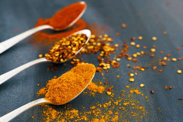 Vintage silver spoons full of paprika, turmeric and chili flakes on a dark background