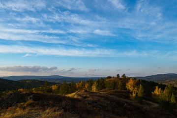 Mountains, autumn forest and blue sky with clouds