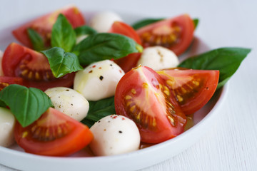 Caprese salad served on a white ceramic plate. White wooden background, high resolution