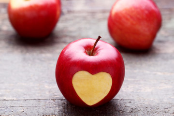 Red apple with cutout heart shape on grey wooden table