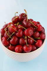 Ripe cherries in a white ceramic bowl. Blue background, high resolution