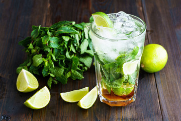Dirty mojito and ingredients (fresh mint, sliced lime) served on a dark wooden board. High resolution.
