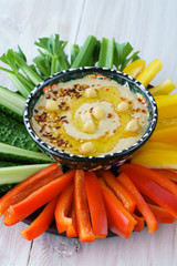 Homemade hummus served in a turkish bowl with fresh bell pepper, cucumer and celery sticks. White wooden table, high resolution