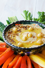 Homemade hummus served in a turkish bowl with fresh bell pepper, cucumer and celery sticks. White wooden table, high resolution