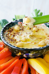 Homemade hummus served in a turkish bowl with fresh bell pepper, cucumer and celery sticks. White wooden table, high resolution
