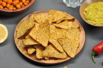 Corn chips nachos on a wooden plate. Next bowl with guacamole sauce. Gray background. View from above. Close-up. Macro photography.