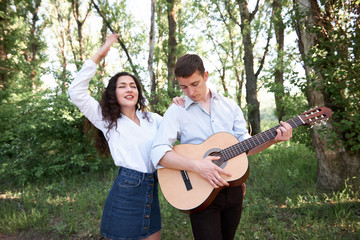 young couple walking in the forest, playing guitar and dancing, summer nature, bright sunlight, shadows and green leaves, romantic feelings