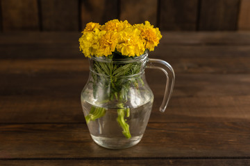 Beautiful yellow autumn flowers in a glass vase on a dark wooden background