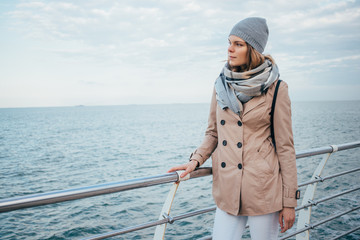 Fototapeta premium Young woman wearing beige coat, scarf, hat and backpack