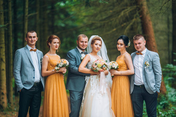 Newly married couple with groomsmen and bridesmaids posing on wedding ceremony. Bride and groom with best friends posing in pine forest. Young people having fun. Wedding day.