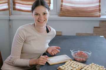 Woman makes dumplings with mince meat, looks at camera and smiles.