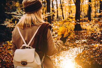 Women holding bouquet of autumn leaves in front of beautiful colorful landscape with a stream and forest in autumn colors. Evening sunlight reflecting on calm water surface