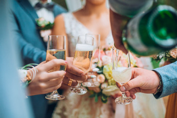 Groomsman opens a bottle of champagne before newlyweds standing in the park. Wedding party in the...