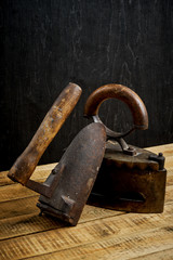 two old rusty iron on a bright wooden table next to a black wall