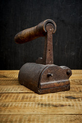 vintage old rusty iron on a bright wooden table next to a black wall