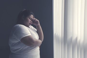 Stressed fat woman standing by the window - obrazy, fototapety, plakaty