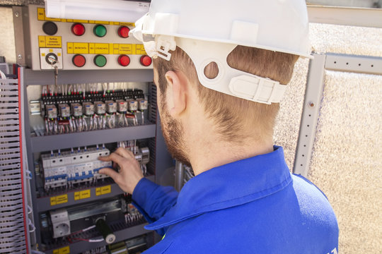 The electrician adjusts the electrical cabinet. engineer in helmet is testing electrical equipment. Maintenance of electric system. Worker diagnostic of automation panel.