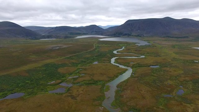 Flying over River in Tundra to Mountains.	The drone from which the video is shot, flies over the tundra to the mountains. A small river flows through the tundra